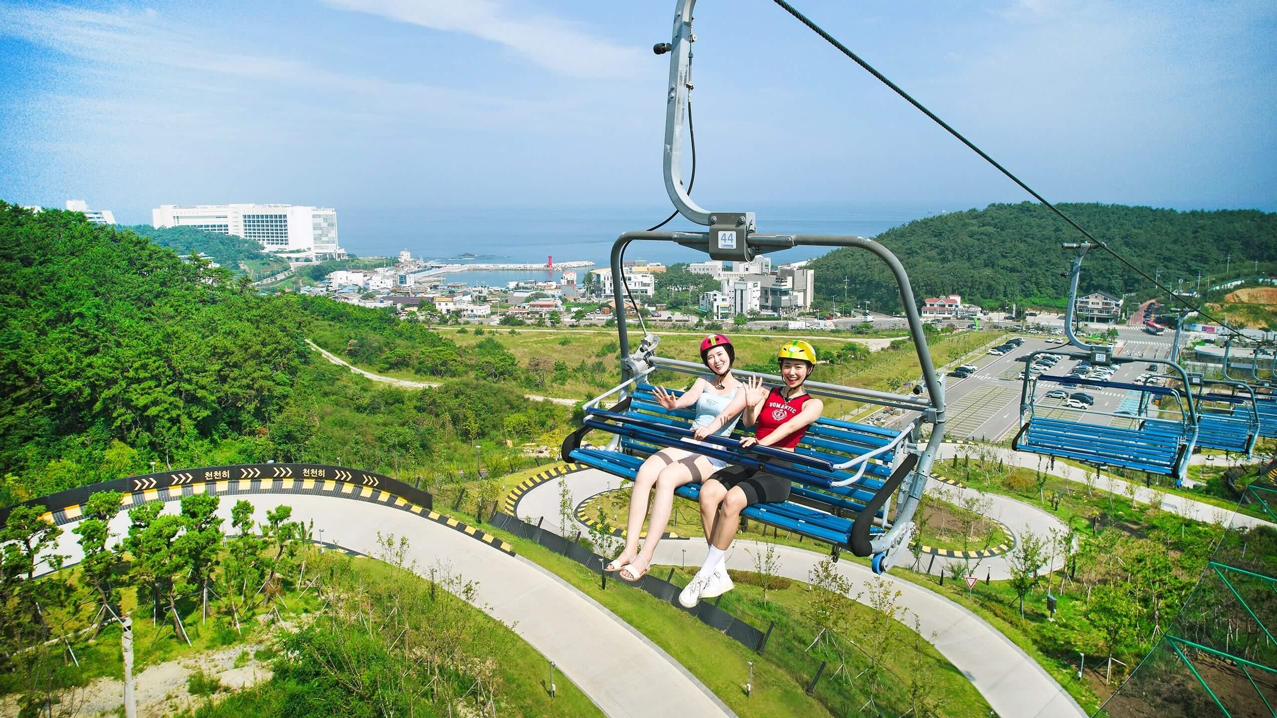Two friends wave while riding the Busan Luge chairlift.