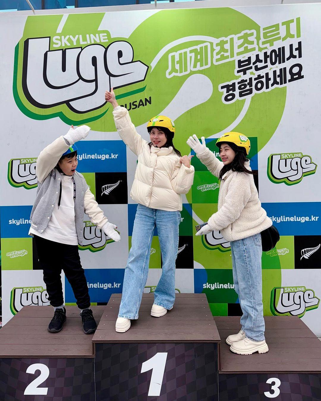 Three young kids stand on the Luge podium at the finish line.
