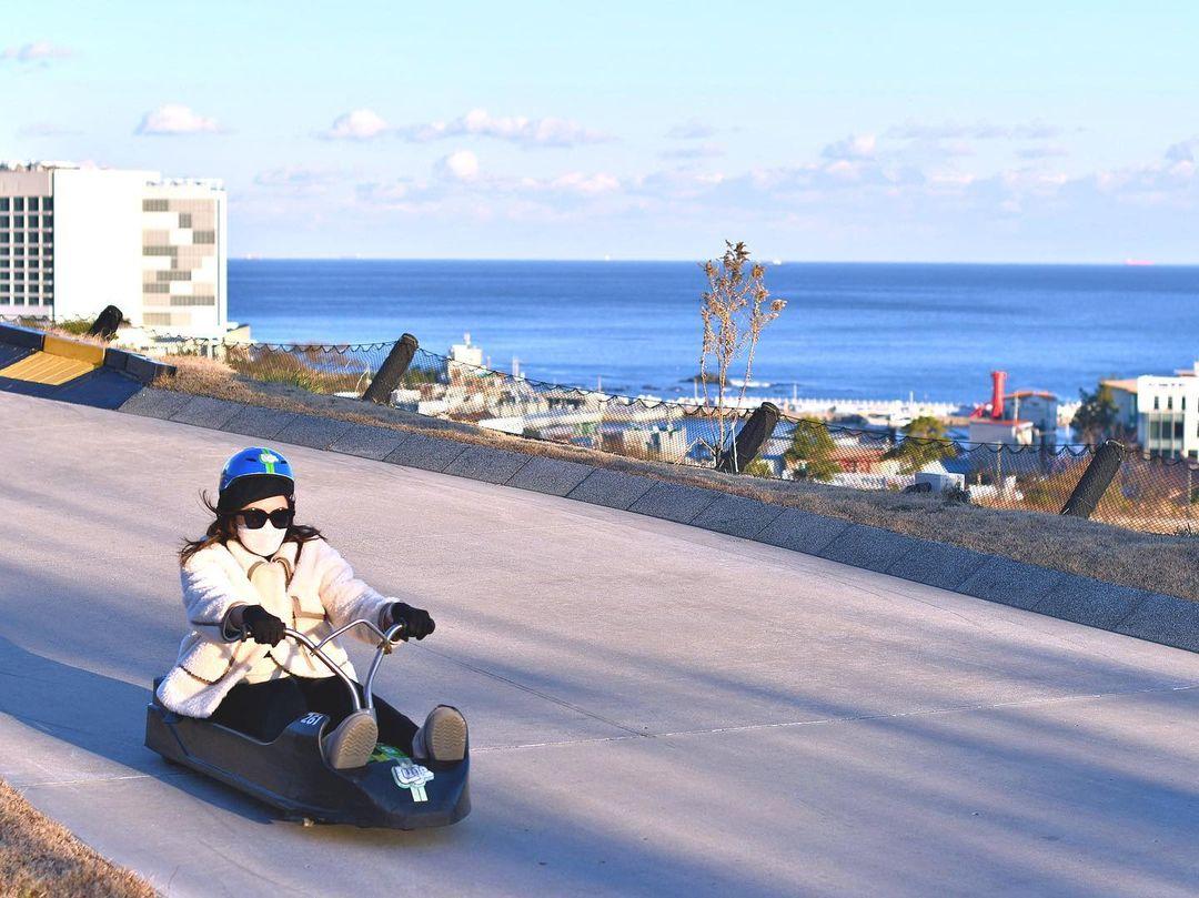 A lady rides the Busan Luge with stunning views of the Dongbusan behind her.