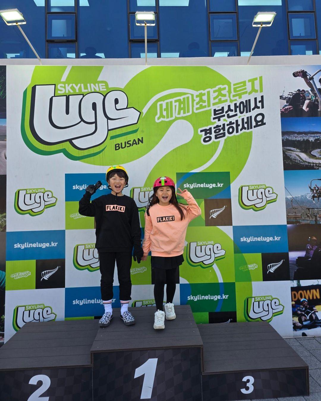 Two kids pose on the Luge podium at Skyline Luge Busan.