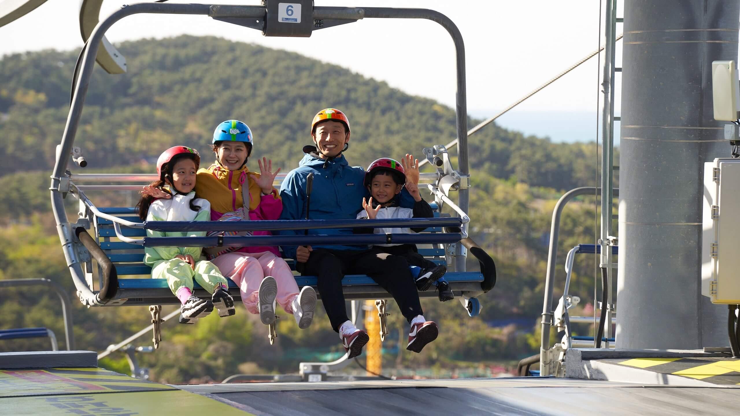 A family of four reaches the top of the Skyline Luge Busan chairlift.