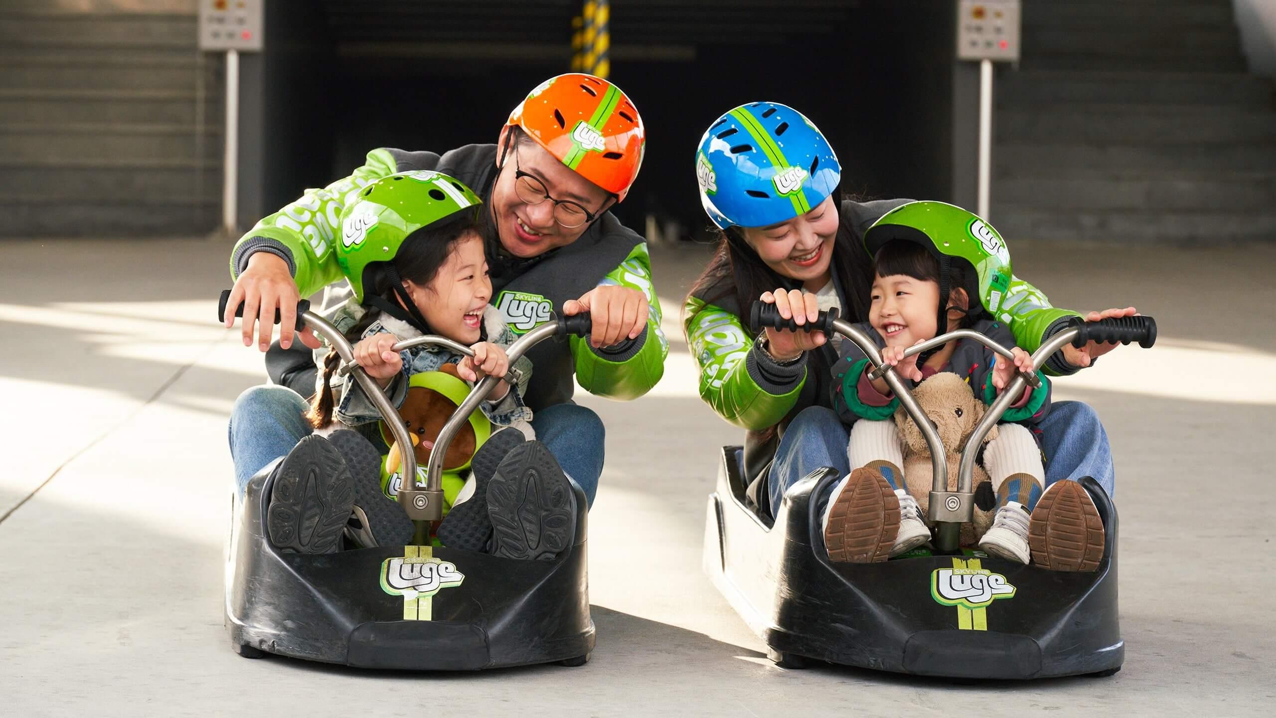Two adults prepare to ride the Luge with small children in the same carts with them.