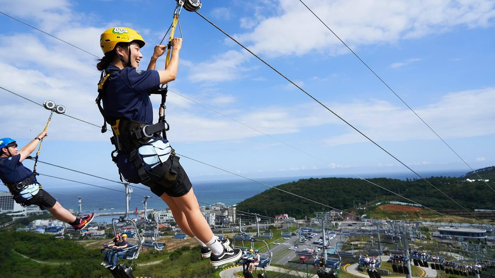 Two friends prepare to ride the Hyfly zipline side by side at Skyline Luge Busan.