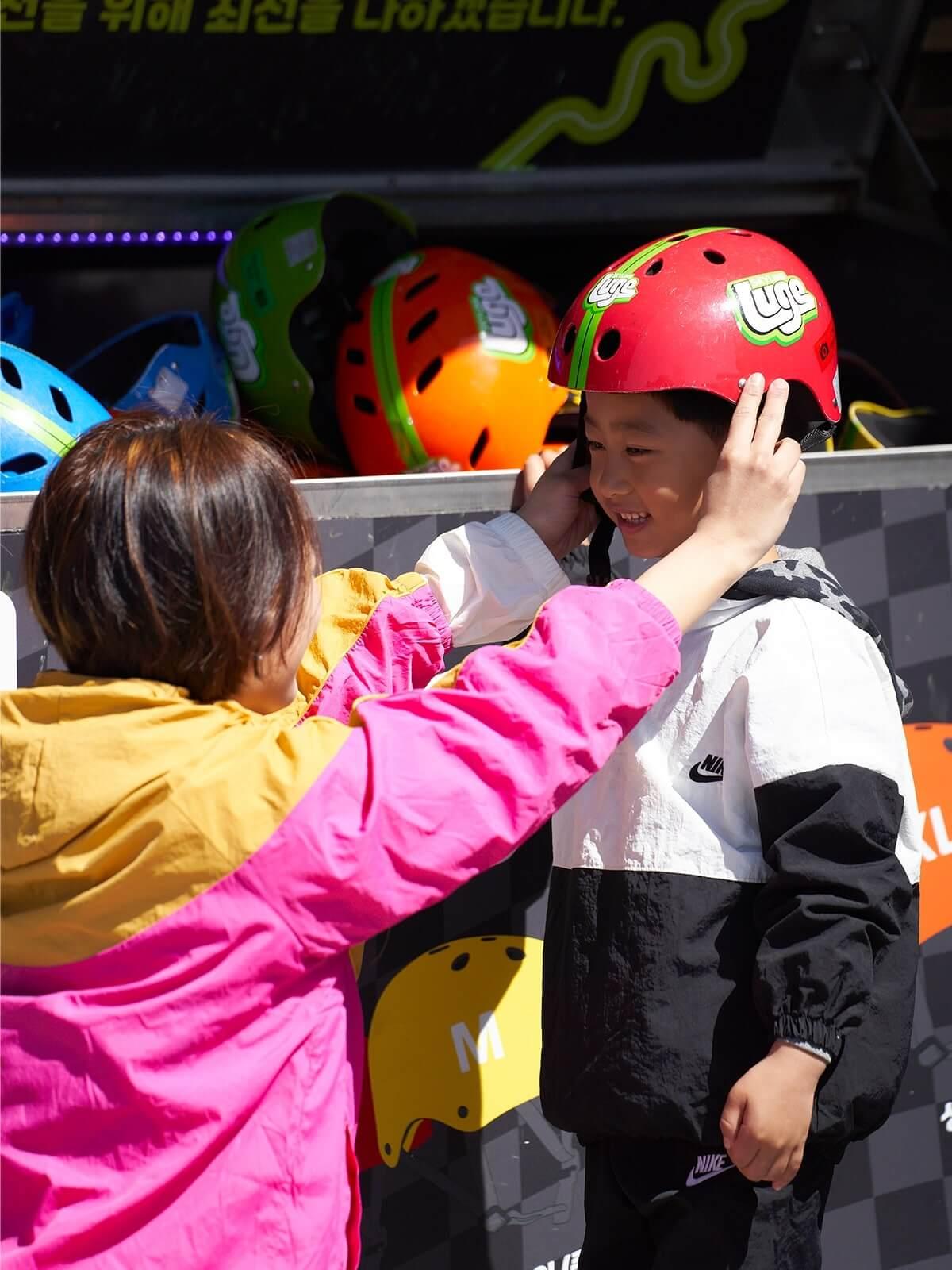 A small child gets his Luge helmet fitted by a parent.