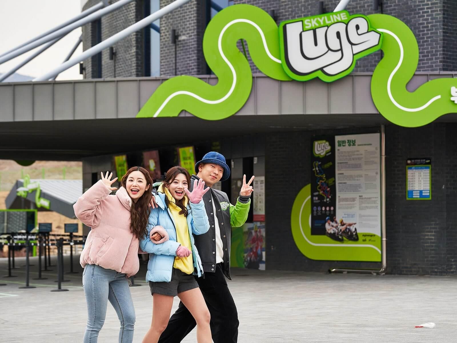 Three friends pose for a photo as they walk past the ticketing building at Skyline Luge Busan.