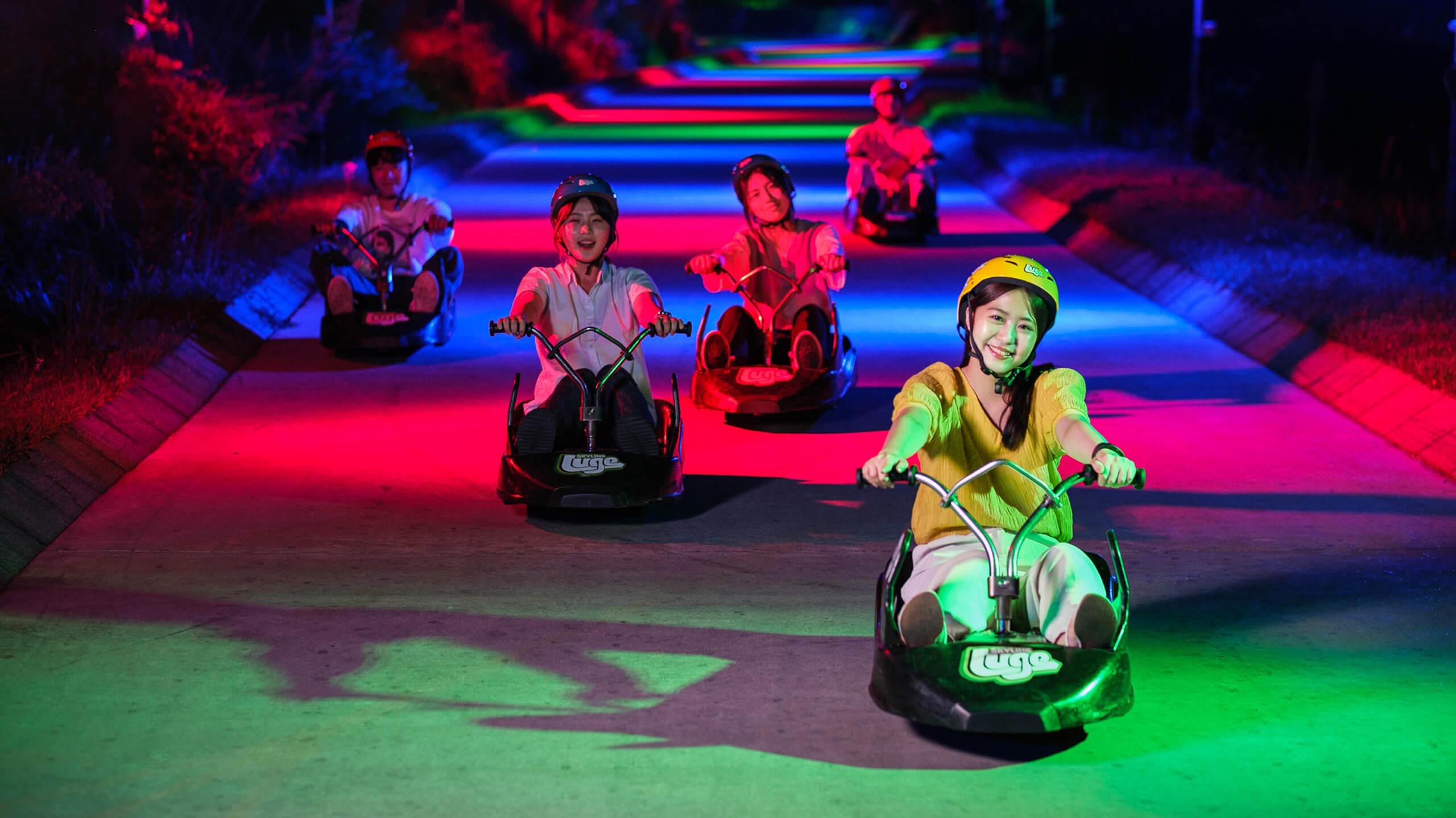 A group of people head down the tracks on the Night Luge at Skyline Luge Tongyeong.