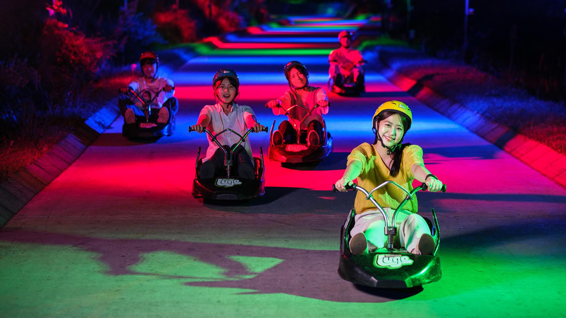 A group of people head down the tracks on the Night Luge at Skyline Luge Tongyeong.
