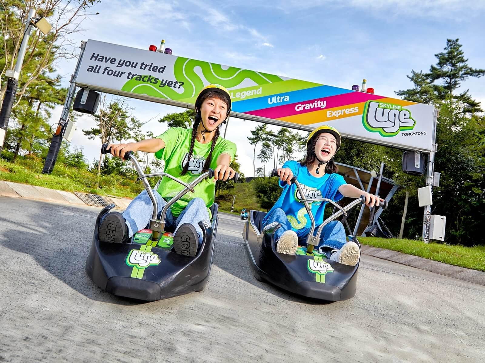 Two girls grin and scream as they ride down a steep section on the track at Skyline Luge Tongyeong.
