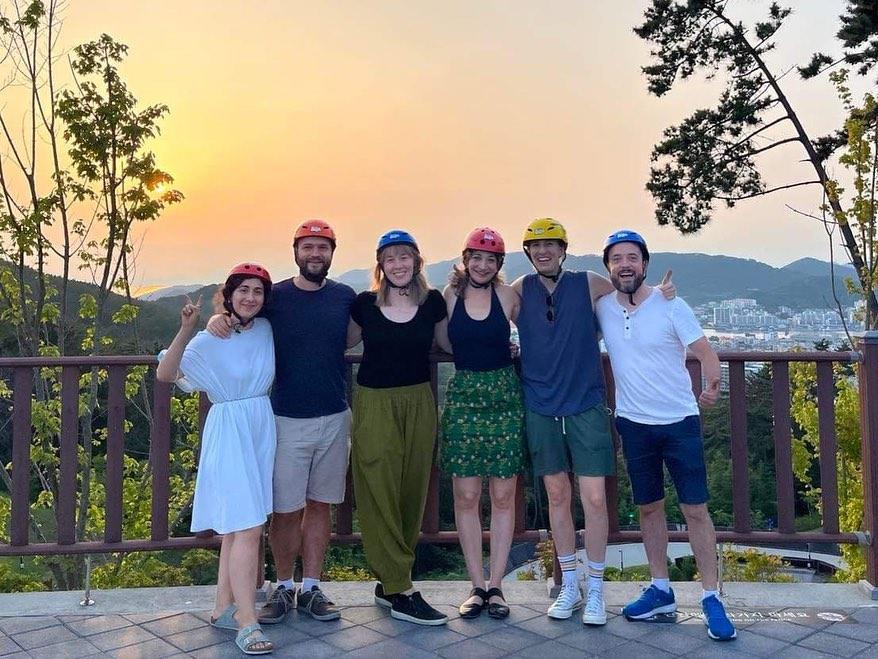 A group of friends pose for a photo at sunset with their Luge helmets on.