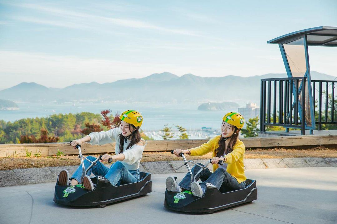 Two friends Luge down the tracks with sweeping ocean views behind.